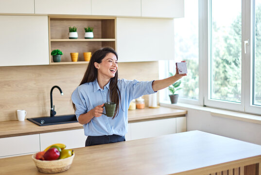 Portrait of a healthy young woman businesswoman enjoying morning in kitchen and taking a selfie with a smart phone at home
