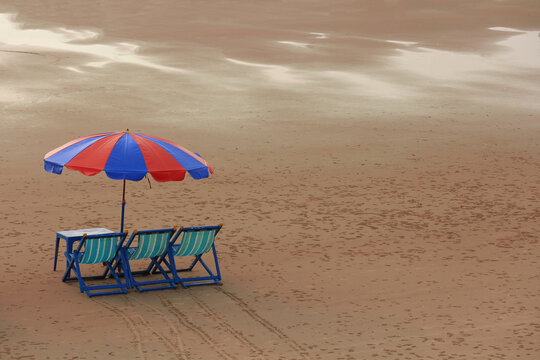 Beach umbrella with empty deck chairs on a sandy shore with footnotes and copy space at sunset.