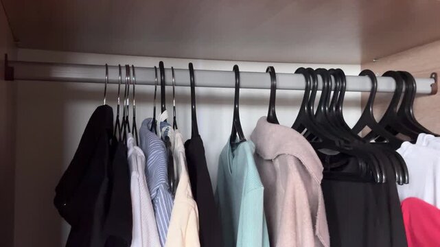 Person removing individual clothes with hangers from wardrobe, sorting garments during decluttering process, home organization, horizontal video