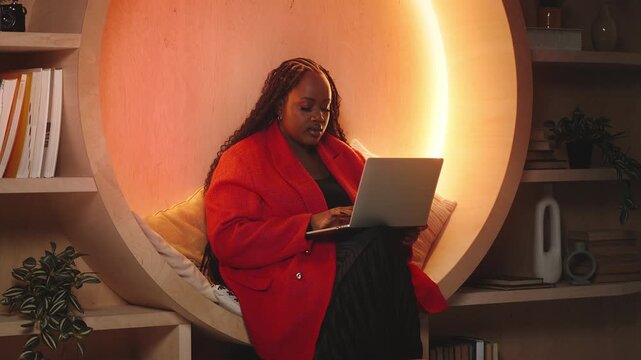 Thoughtful Black female AI developer works on laptop in modern library