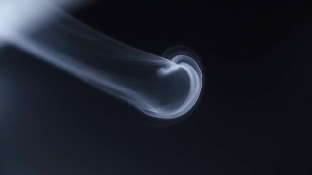 Slow motion static shot of smoke plume curling and spiraling into a trailing swirl against dark studio background