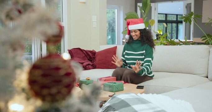 African American woman checking smartphone wrapping pink gift with ribbon on sofa wearing Santa hat