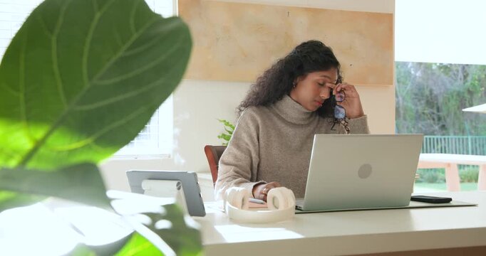 African American woman home office typing on laptop rubbing eyes answering ringing phone refocusing