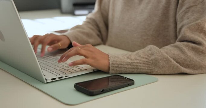 African American woman wearing tan sweater typing on laptop at home hearing call leaving voicemail