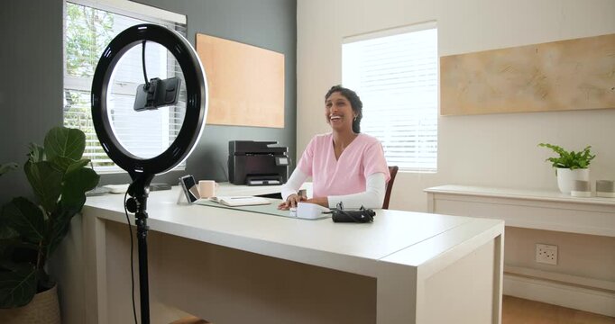 African American woman in pink scrubs recording with ring light phone at desk, showing device