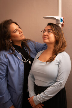 A female doctor checks a standing patient's height on a stadiometer during a routine medical examination in a clinic.