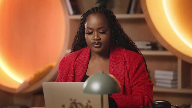 African American female journalist writes article on laptop in modern office