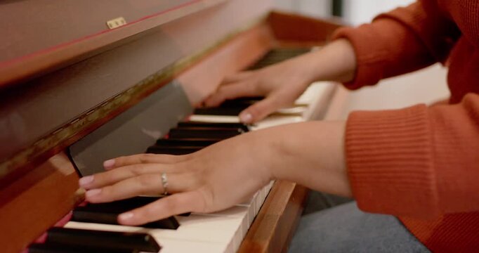 Hovering hands are settling onto keys, pressing chords and melodies at upright piano for practice