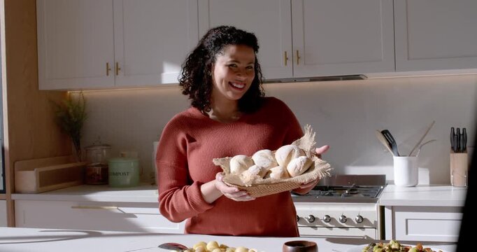 African American woman in rust sweater presenting basket of rolls at kitchen island, camera rolling
