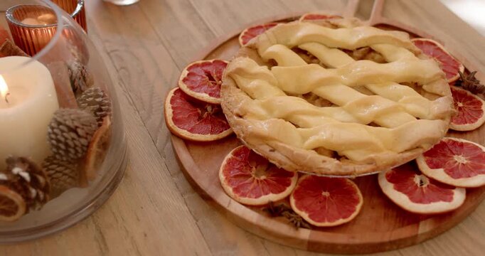 Camera is shifting closer as candle is igniting, warming lattice pie on wooden tabletop with citrus