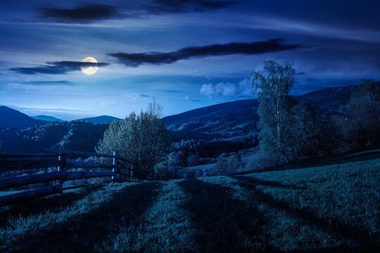 mountainous rural landscape in spring at night. mysterious view of valley fields. full moon over alpine meadow. carpathian mountains countryside with forest near pasture. agricultural fantasy