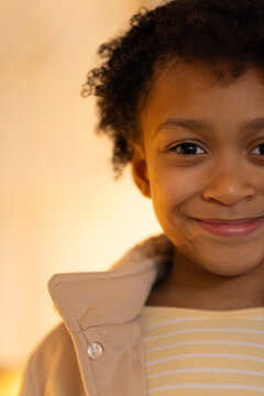 African American child smiling, wearing beige coat with button and yellow striped shirt in studio