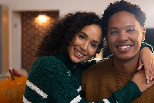 African couple sitting on sofa at home, woman wearing green sweater leaning on man, pumpkin left