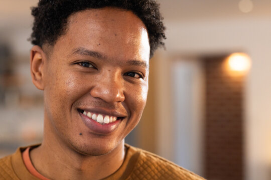 Adult African American man smiling, looking at camera at home with wall sconce, in quilted sweater