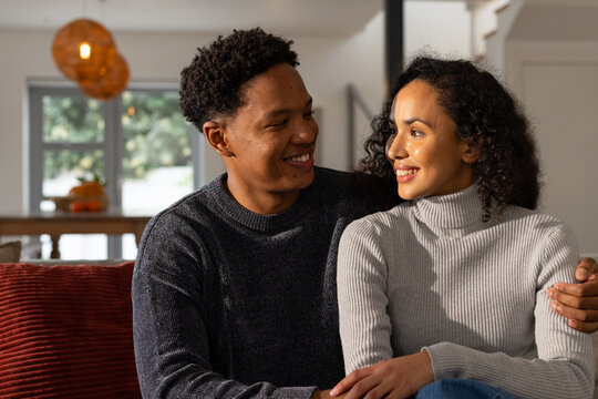 African American couple sitting on red sofa, sharing smiles with amber light, pumpkin bowl