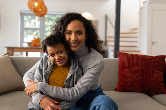 Mother and daughter hugging, smiling and sitting on light gray sofa with bowl of oranges