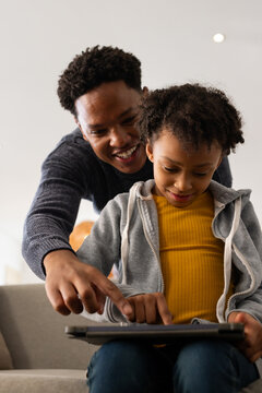 African male caregiver and female youth in mustard top leaning on couch at home, tapping tablet
