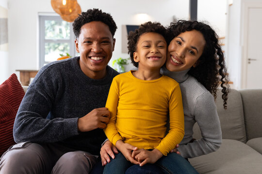African American family sitting on gray sofa with red pillow in living room, smiling and leaning