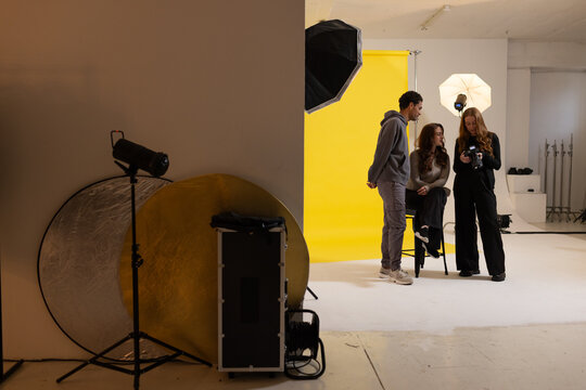 Diverse coworkers reviewing camera footage on studio set with yellow backdrop and gear, copy space