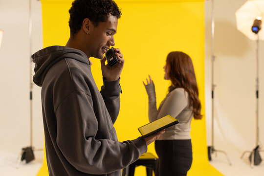 Diverse crew directing by yellow backdrop speaking into radio with tablet, model posing, copy space