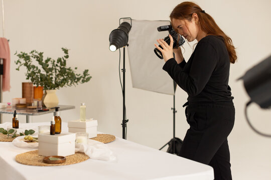 Female photographer holding DSLR camera, framing table products in studio with softbox, copy space