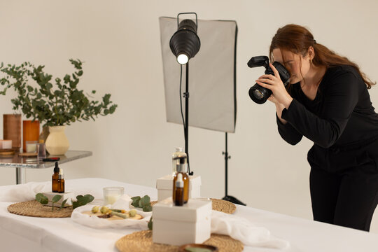 Adult female camera operator wearing black leaning shooting table with DSLR and softbox, copy space