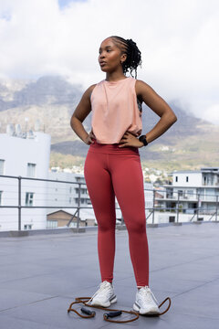African American woman standing on rooftop wearing peach top and red leggings with jump rope