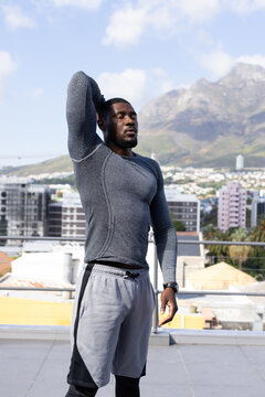African man stretching on rooftop terrace in city, wearing compression top and smartwatch