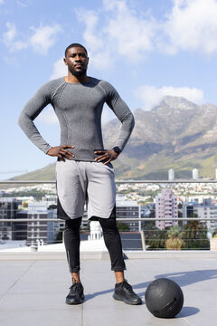 African man on roof standing, city, mountain view, in compression, smartwatch, black medicine ball