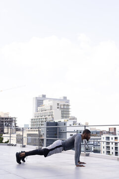Mid adult man in gray athletic top holding high-plank on rooftop with railing, crane, copy space