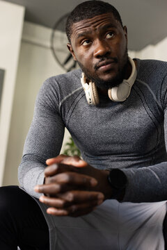 Man sitting in home corner wearing fitted top, headphones and smartwatch looking up