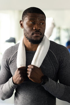African American man holding white towel, wearing grey compression top and smartwatch in gym