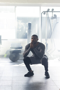 African American man doing deep squat on rubber gym floor near bench wearing gray compression top