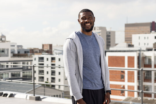 Mid-adult man standing on rooftop terrace in city, wearing gray hoodie and checking smartwatch