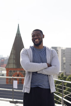 African man wearing gray hoodie standing on rooftop by railing note with church steeple