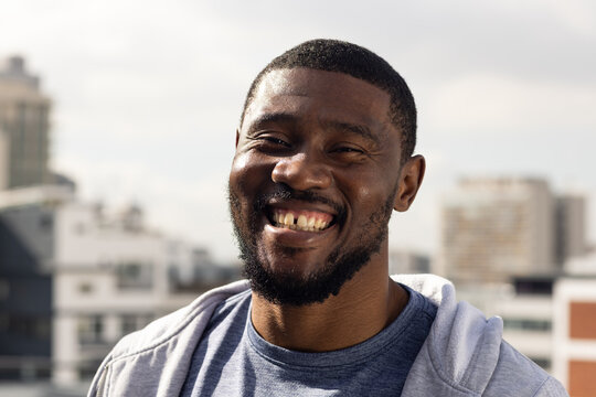 African American man smiling, standing on rooftop wearing gray hoodie and blue t-shirt