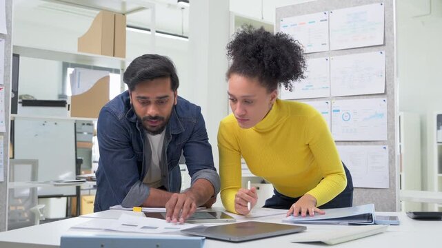 Three colleagues huddled closely together, reviewing a data analytics chart on a tablet screen, deeply focused and collaborative moment in a busy modern office.