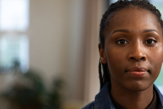 Adult African woman posing in denim jacket by window, curtains and potted plant, copy space