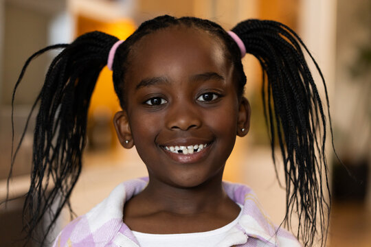 African American girl smiling at home wearing light purple top, pink hair ties and stud earrings