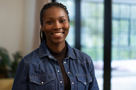 African woman smiling and posing in lounge, wearing denim shirt, dark turtleneck with grid door