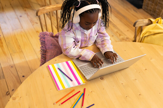 African American child female typing on silver laptop at home study table with white headphones