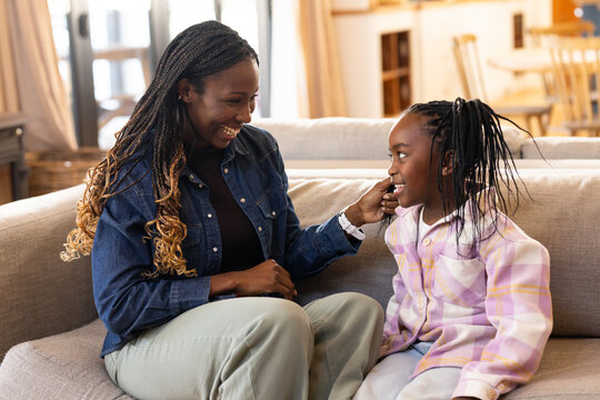 African mother and child on sofa at home smiling, reaching, wearing jean jacket and plaid shirt