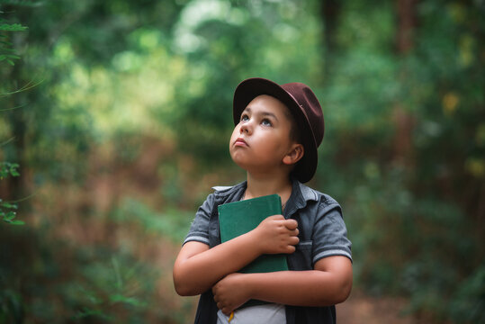 Inspired boy hugging a book looking up in a forest. Inspired little boy hugging a book to his chest and looking up with wonder in a green summer forest.
