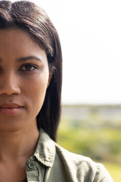 African American woman looking at camera in park wearing olive shirt, stud earring, copy space