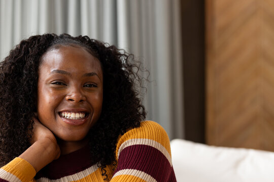 African adult woman smiling and resting head while wearing ribbed sweater on light-colored sofa