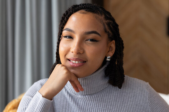 Adult woman sitting, resting chin on hand at home, wearing gray turtleneck and silver hoops