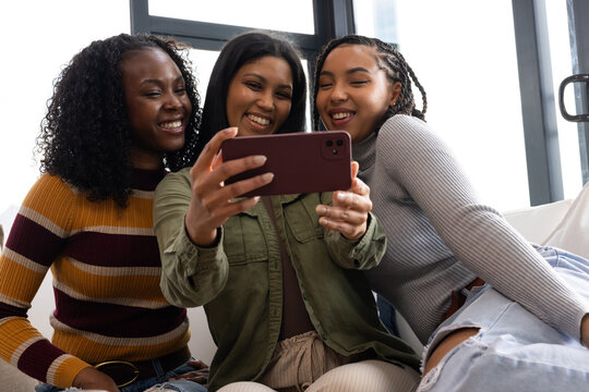 African American women sitting on couch taking selfie by window, holding burgundy case