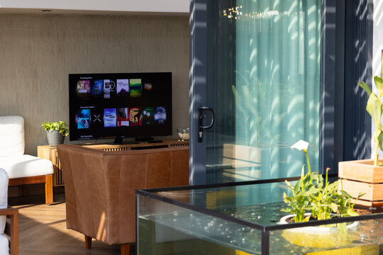 TV sitting on wood console with brown leather chair near glass door, sunlight reflecting