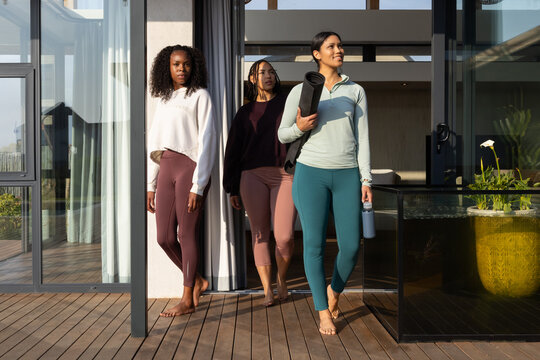 African American women in leggings walking on wooden deck carrying rolled yoga mat and water bottle