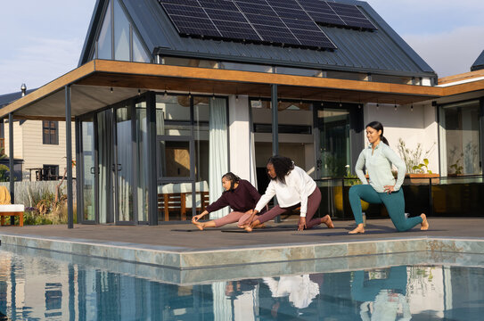 African American women stretching on wooden pool deck at modern house, wearing athletic clothes